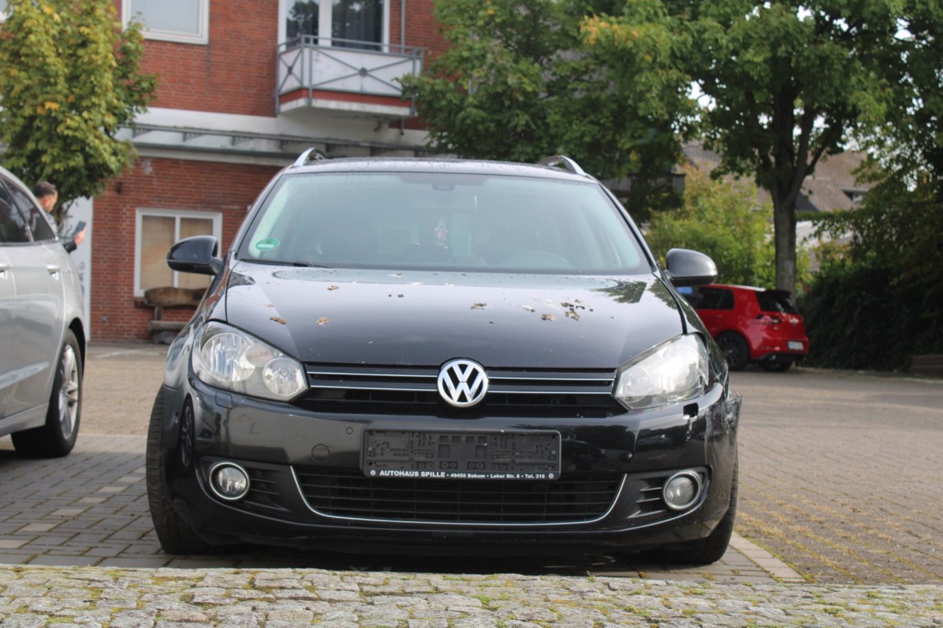 Schwarzer Volkswagen Golf, Frontansicht, geparkt auf einem Platz mit Bäumen im Hintergrund.